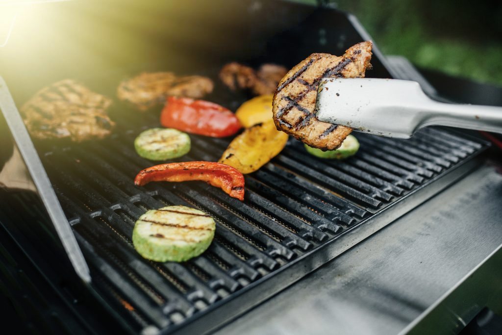 Young man grilling some meat and vegetable on huge grill.